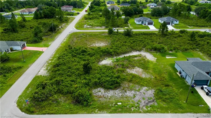 Cleared building envelope on a corner lot featuring street frontage, surrounding foliage, and proximity to existing residences