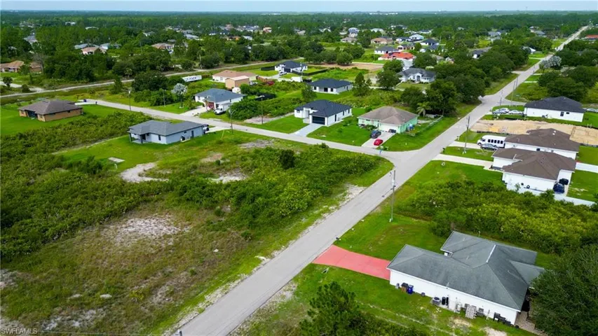 Aerial perspective showcasing a residential area with multiple single-story homes, paved streets, and a mix of developed and undeveloped lots