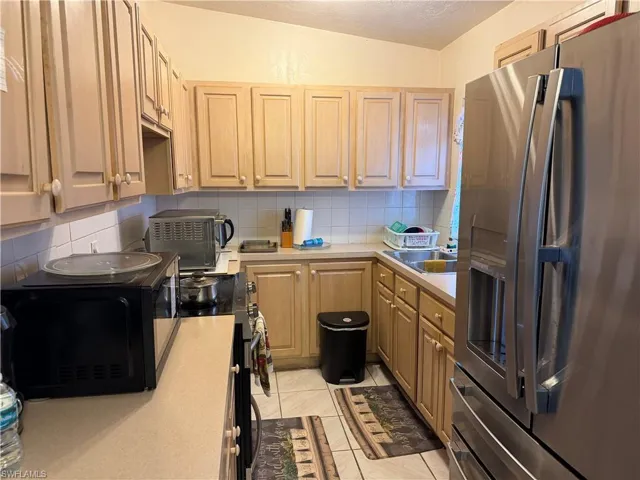 Kitchen featuring stainless steel appliances, light countertops, decorative backsplash, light tile patterned floors, and light wood finish cabinetry