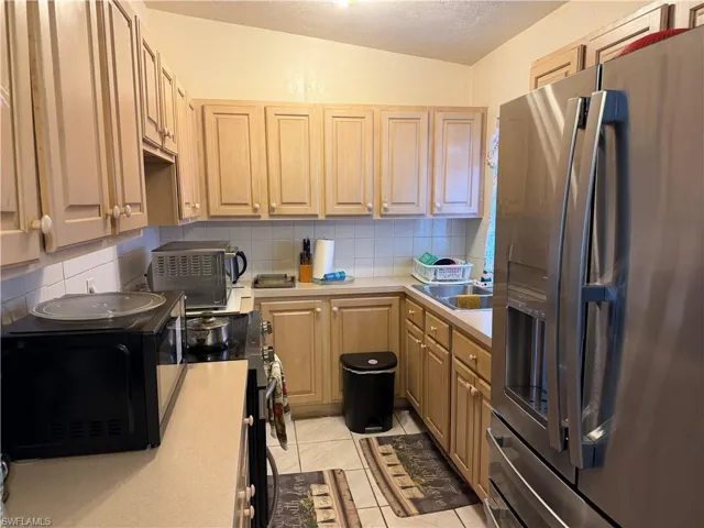 Kitchen featuring stainless steel appliances, light countertops, decorative backsplash, a textured ceiling, and light tile patterned floors