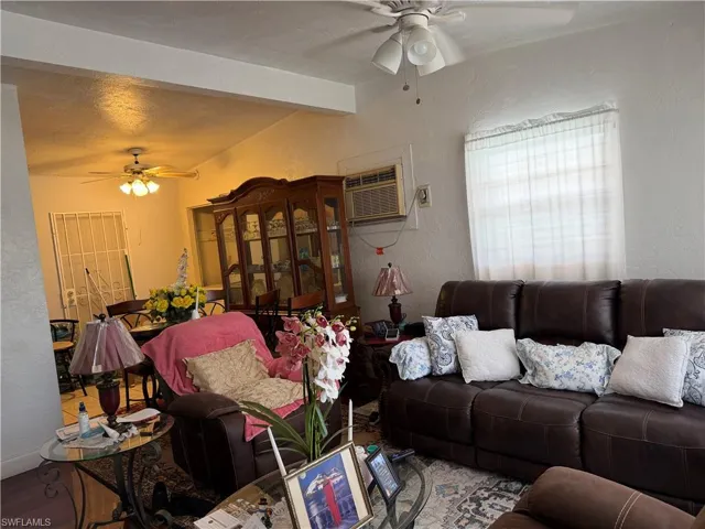 Living area featuring a ceiling fan, a textured wall, beam ceiling, and wood finished floors