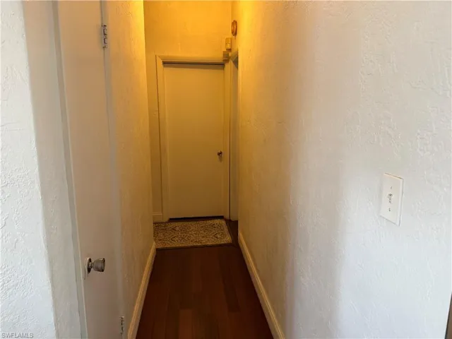 Corridor featuring a textured wall and dark wood finished floors