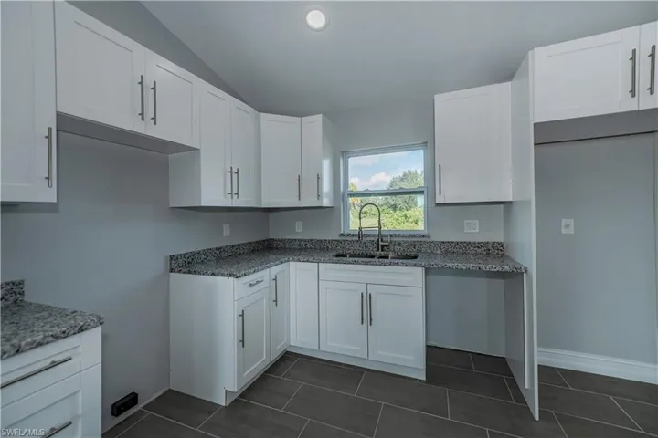 Kitchen featuring dark tile floors, sink, stone countertops, and white cabinetry