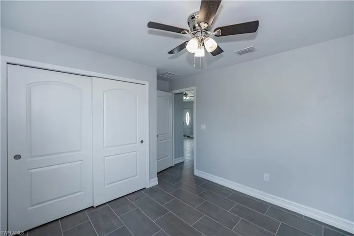 Unfurnished bedroom with ceiling fan, a closet, and dark tile floors