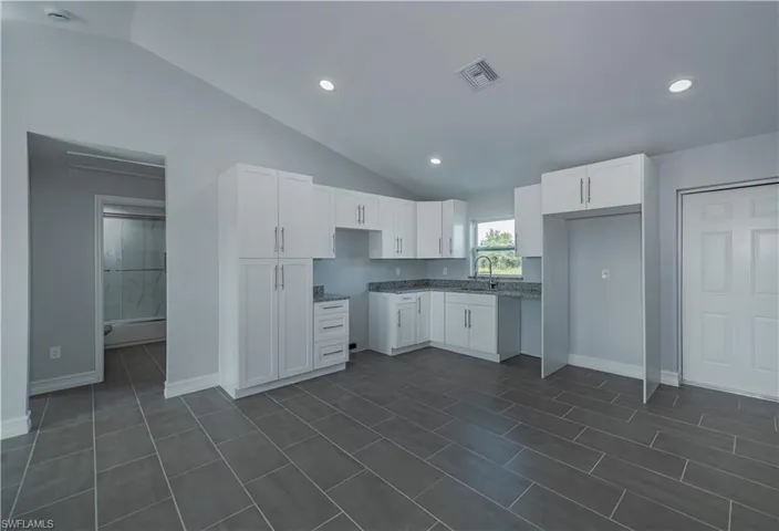 Kitchen with sink, white cabinets, dark tile flooring, and stone countertops