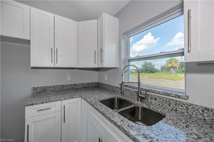 Kitchen with light stone counters, vaulted ceiling, white cabinets, and sink