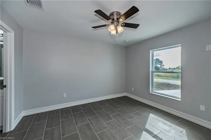 Empty room featuring a wealth of natural light, ceiling fan, and dark tile floors