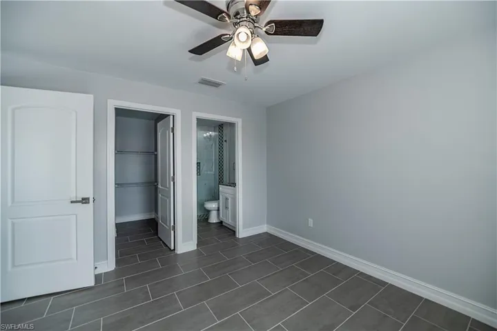 Unfurnished bedroom featuring dark tile flooring, ceiling fan, a walk in closet, and connected bathroom