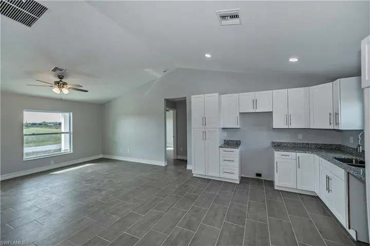 Kitchen with ceiling fan, dark tile floors, sink, lofted ceiling, and white cabinetry
