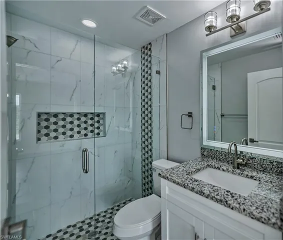 Bathroom featuring a shower with shower door, toilet, and large vanity
