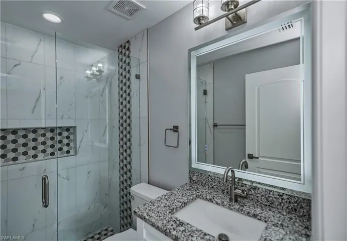 Bathroom featuring walk in shower, vanity, and toilet
