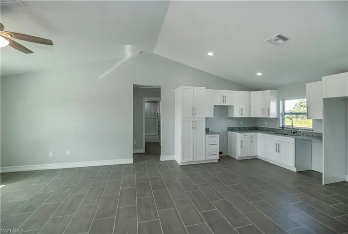 Kitchen with ceiling fan, sink, vaulted ceiling, and white cabinets