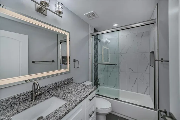 Full bathroom with shower / bath combination with glass door, tile flooring, vanity, and toilet