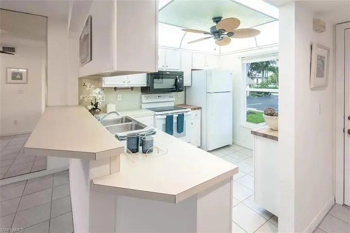 Kitchen with white appliances, white cabinets, kitchen peninsula, light tile patterned flooring, and ceiling fan