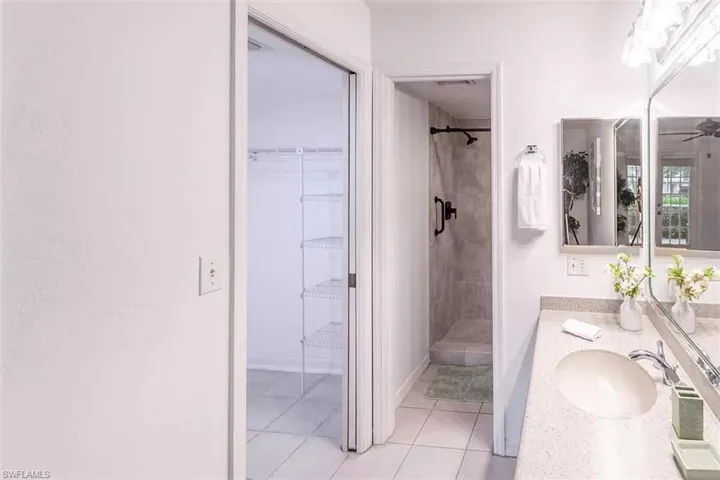 Bathroom with tiled shower, vanity, ceiling fan, and tile patterned flooring