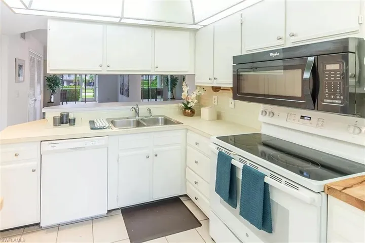Kitchen featuring sink, white cabinets, white appliances, and light tile patterned floors