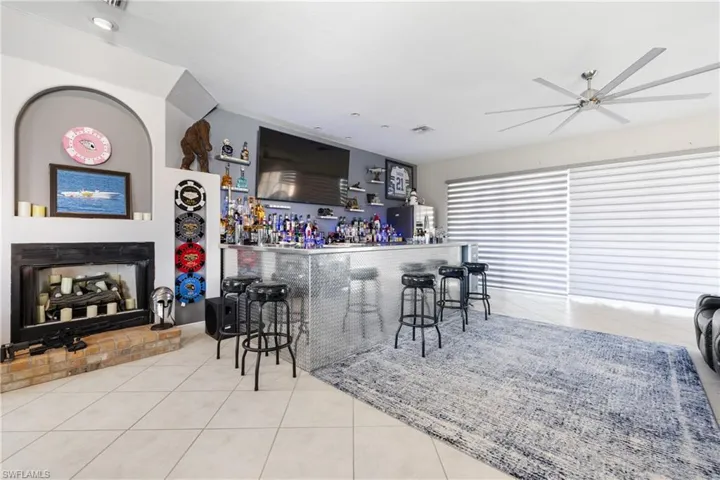 Bar featuring light tile patterned floors, a ceiling fan, a fireplace with raised hearth, and stainless steel refrigerator with ice dispenser