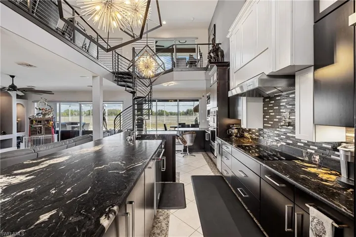 Kitchen featuring dark stone counters, a high ceiling, open floor plan, light tile patterned floors, and a ceiling fan