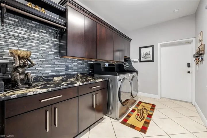 Laundry area with light tile patterned floors, washing machine and clothes dryer, and cabinet space