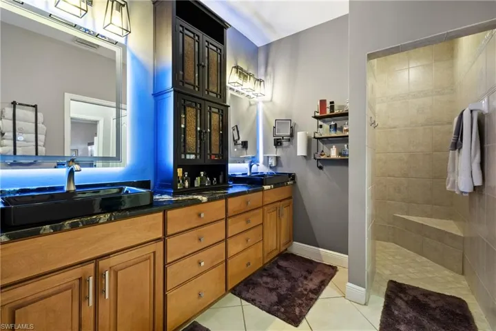 Full bathroom with double vanity, walk in shower, and light tile patterned flooring