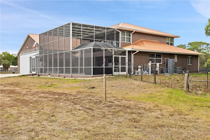 Rear view of property featuring a lanai, a fenced backyard, a sunroom, and a metal roof