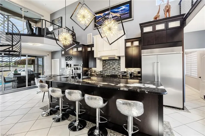 Kitchen with a kitchen bar, stainless steel appliances, glass fronted cabinets, a spacious island, and a high ceiling