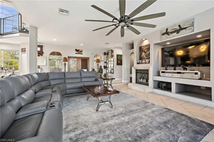 Living room featuring built in shelves, light tile patterned floors, recessed lighting, a glass covered fireplace, and a ceiling fan