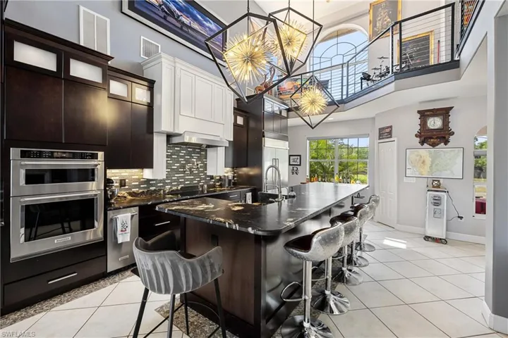 Kitchen with an island with sink, hanging light fixtures, a breakfast bar area, decorative backsplash, and glass insert cabinets