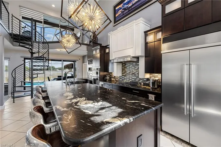 Kitchen with glass insert cabinets, stainless steel appliances, a breakfast bar area, a large island with sink, and hanging light fixtures