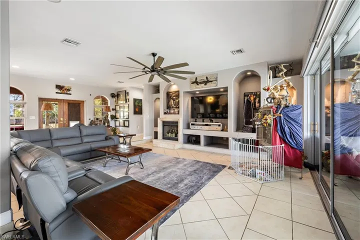 Living room featuring light tile patterned floors, arched walkways, ceiling fan, built in features, and a fireplace with raised hearth
