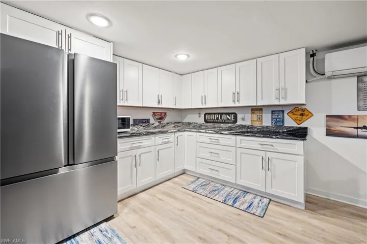 Kitchen with freestanding refrigerator, white cabinetry, light wood-type flooring, dark stone counters, and recessed lighting