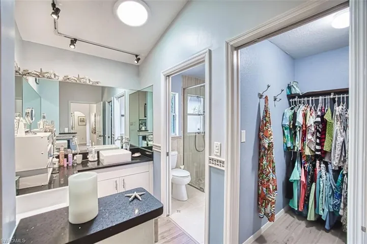 Full bathroom featuring tiled shower, vanity, light wood-style floors, a walk in closet, and rail lighting