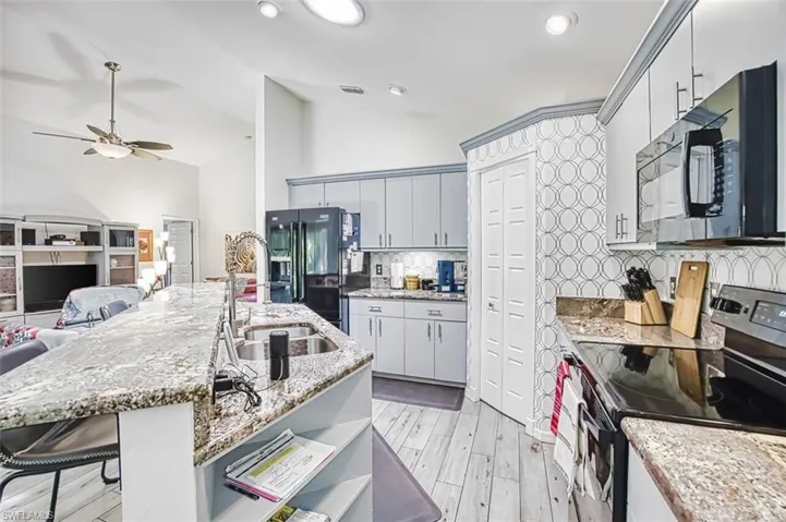 Kitchen featuring black appliances, a breakfast bar, light wood-style flooring, light stone counters, and vaulted ceiling