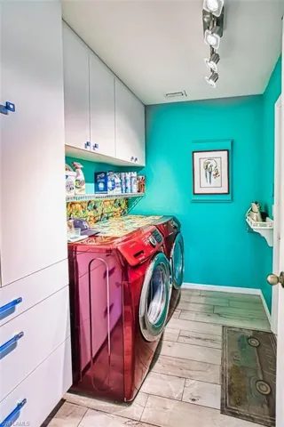 Laundry area featuring washing machine and dryer, cabinet space, light wood-type flooring, and rail lighting