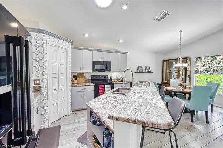 Kitchen with black appliances, a kitchen bar, an island with sink, light stone countertops, and light wood finished floors