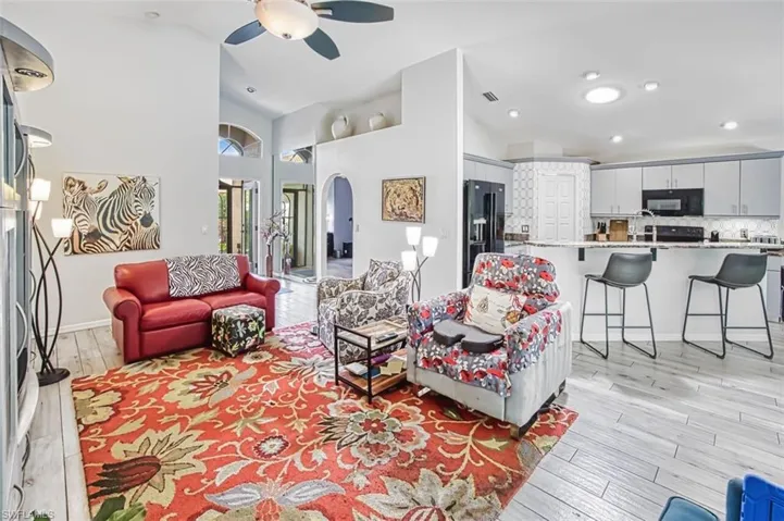 Living room featuring light wood finished floors, arched walkways, ceiling fan, lofted ceiling, and recessed lighting