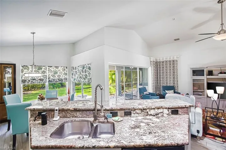 Kitchen with light stone countertops, light wood-style flooring, decorative light fixtures, open floor plan, and vaulted ceiling