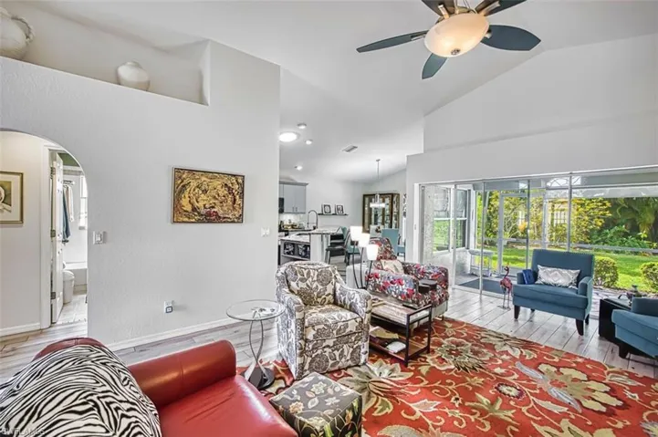 Living area featuring arched walkways, light wood-type flooring, lofted ceiling, and a ceiling fan