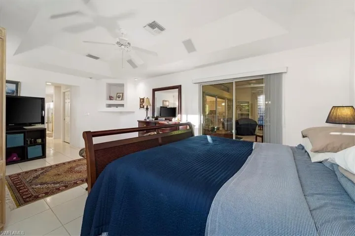 Bedroom with light tile flooring, ceiling fan, a raised ceiling, and access to outside