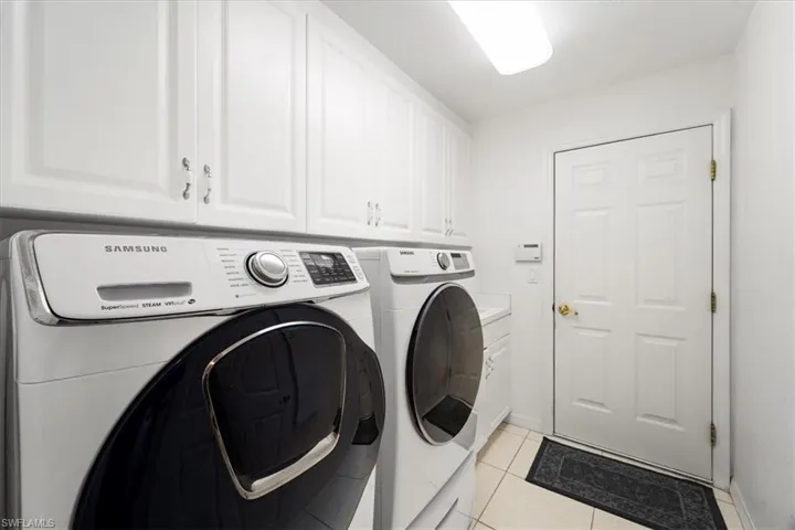 Clothes washing area with independent washer and dryer, cabinets, and light tile floors