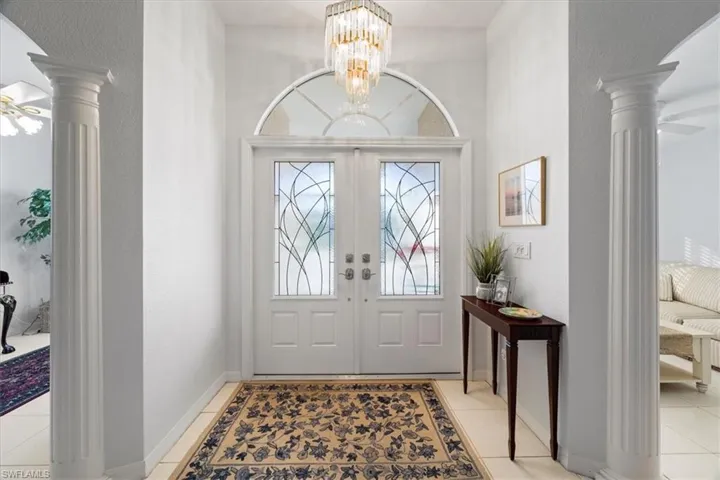 Foyer entrance featuring ceiling fan with notable chandelier, french doors, light tile flooring, and decorative columns
