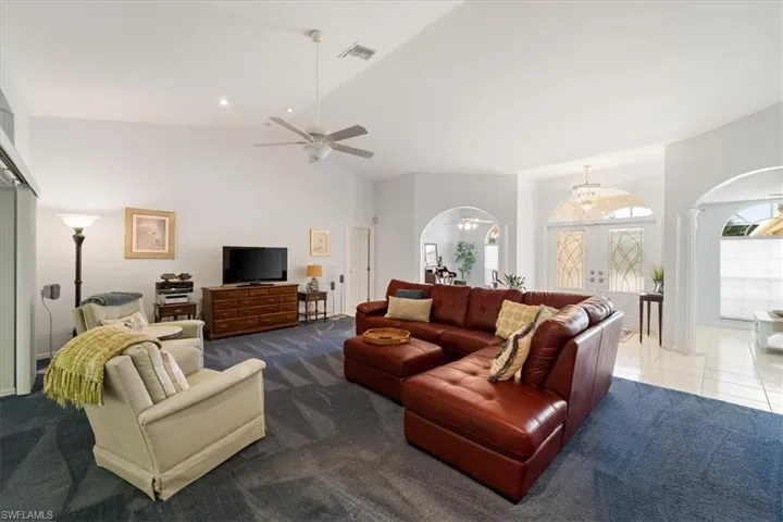 Living room with high vaulted ceiling, ceiling fan, carpet floors, and french doors