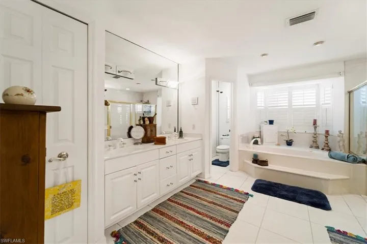 Bathroom featuring a bath, double vanity, tile floors, and toilet