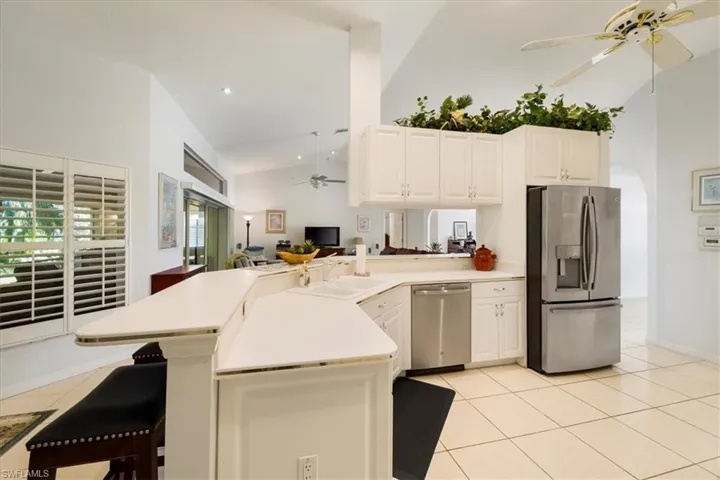 Kitchen with kitchen peninsula, stainless steel appliances, ceiling fan, high vaulted ceiling, and light tile floors