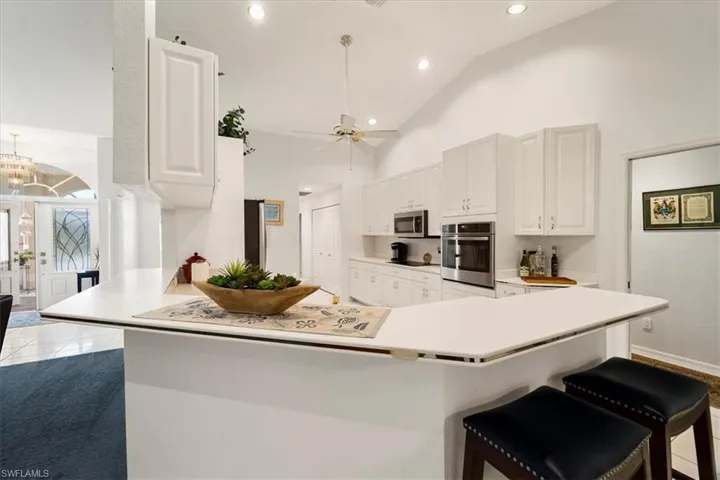 Kitchen with ceiling fan with notable chandelier, kitchen peninsula, light colored carpet, appliances with stainless steel finishes, and a breakfast bar