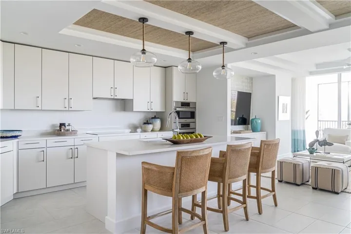 Kitchen featuring a kitchen bar, a kitchen island with sink, light tile patterned floors, open floor plan, and white cabinetry weathered wood inlays and beams in the kitchen