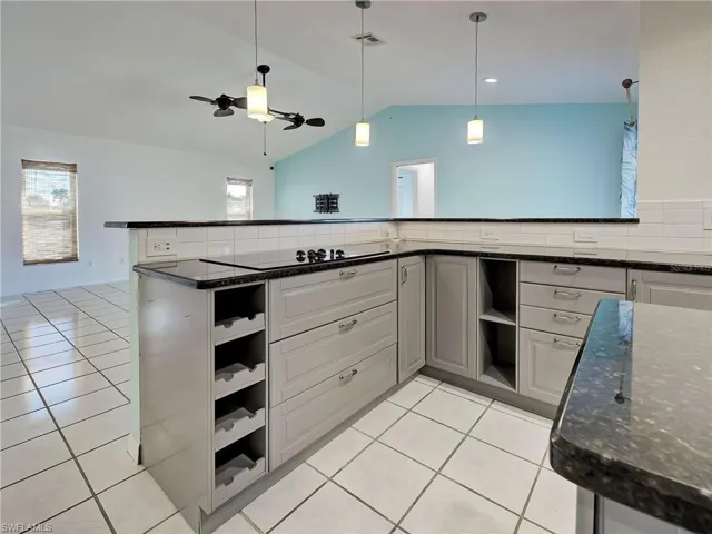 Kitchen with open shelves, dark stone counters, light tile patterned floors, a ceiling fan, and decorative light fixtures