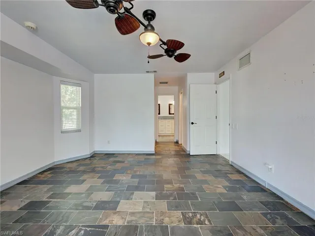 Unfurnished bedroom with ceiling fan, ensuite bath, and dark stone finish flooring