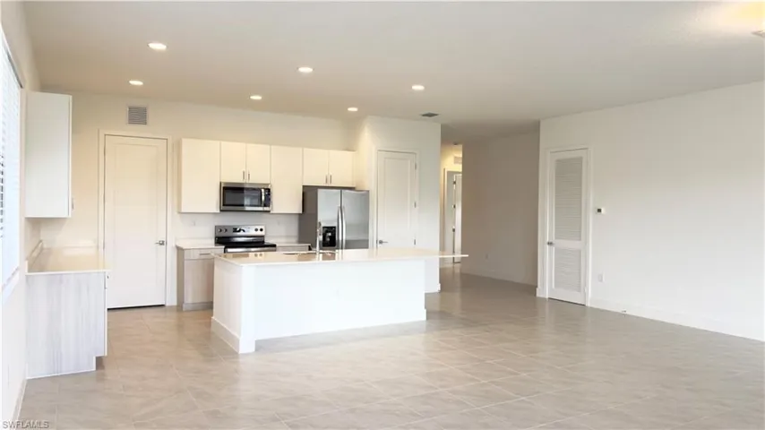 Kitchen with white cabinets, appliances with stainless steel finishes, a kitchen island with sink, recessed lighting, and open floor plan