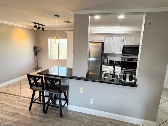Kitchen with stainless steel appliances, a peninsula, a breakfast bar, crown molding, and white cabinets